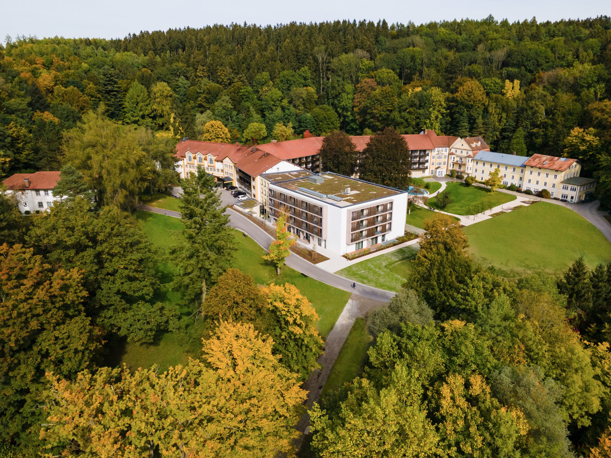 Das Foto zeigt eine Luftaufnahme, der Klinik Wartenberg von Südwesten aus. Mittig ist der Neubau der Klinik zu sehen und dahinter erstreckt sich das weitere Gebäude. Links im Bild erkennt man das Haus Irmgard. Die Klinik ist umgeben von einem grünen Park- und Waldareal.