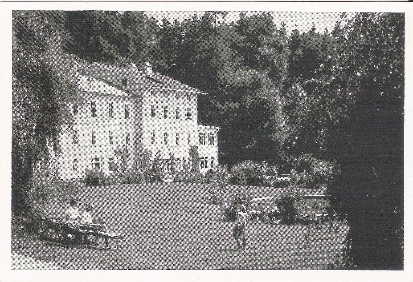 Historische schwarz-weiß Aufnahme einer Postkarte, auf der man das Altgebäude sowie die Parkanlage der Klinik Wartenberg erkennen kann. Personen sitzen auf liegen im Park. Im Hintergrund erkennt man den Klinikwald.