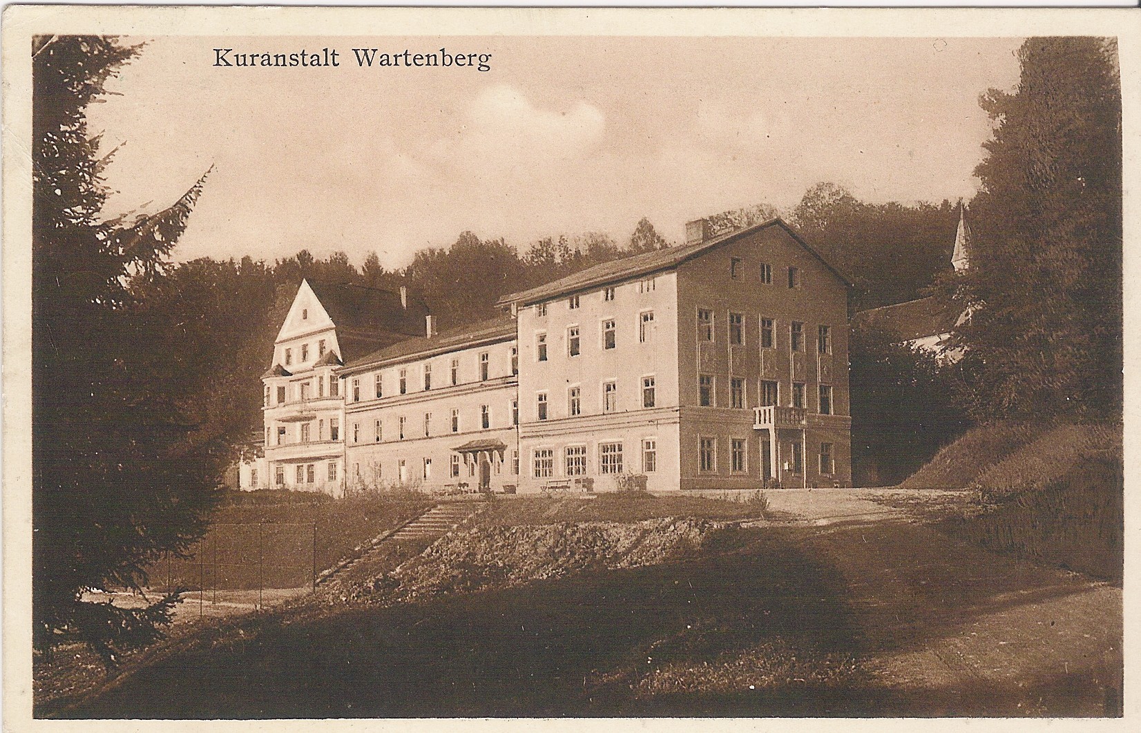 Historische schwarz-weiß Aufnahme einer Postkarte von 1928, auf der man das Altgebäude der Klinik Wartenberg erkennen kann. Im Hintergrund sieht man die heute nicht mehr existierende Bründlkirche.