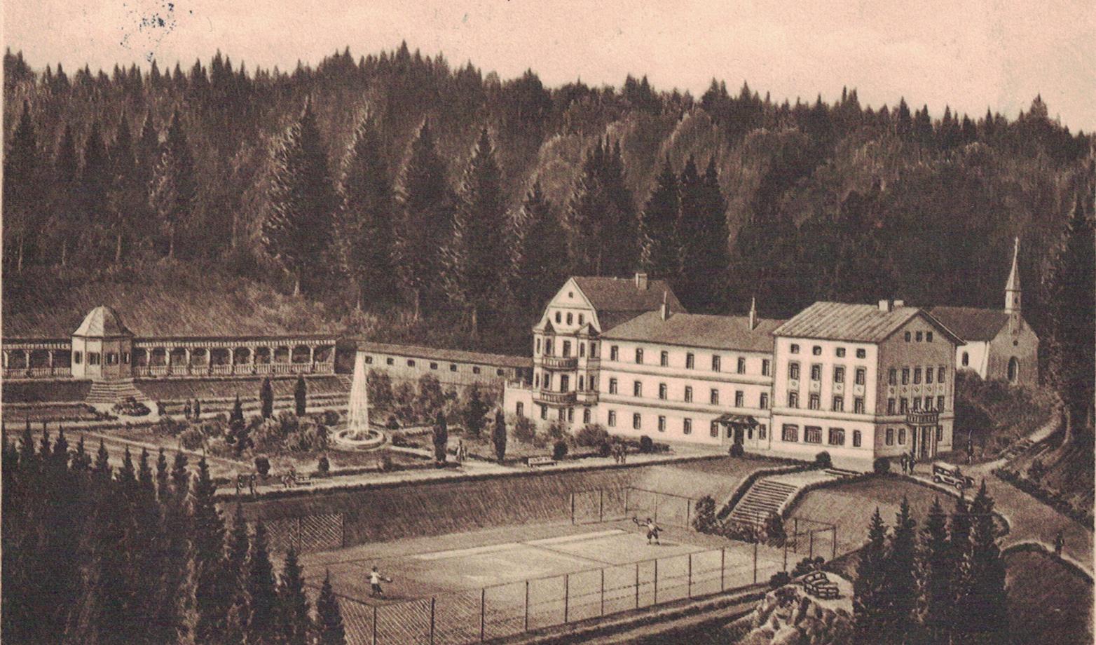 Historische schwarz-weiß Aufnahme einer Postkarte von 1930, auf der man das Altgebäude der Klinik Wartenberg sowie die heute nicht mehr existierende Liegehalle, Bründlkirche und den Tennisplatz erkennen kann. In der Mitte des Geländes sieht man den Springbrunnen. Im Hintergrund der Klinik weit.