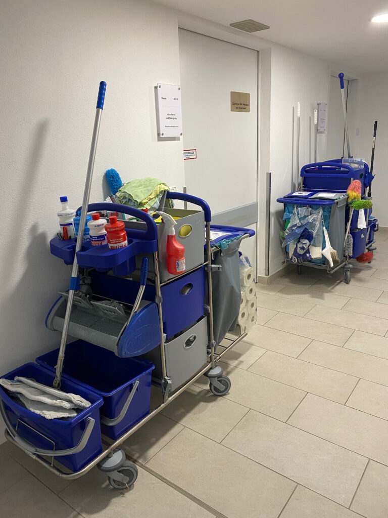 Auf dem Foto sieht man zwei Reinigungswagen mit Putzutensilien im Flur vor der Wäscherei der Klinik Wartenberg.