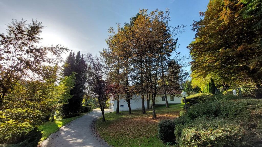 Foto von Haus Irmgard auf dem Klinikgelände im Herbst. Laub liegt auf dem Boden, Sonne scheint von der Seite.
