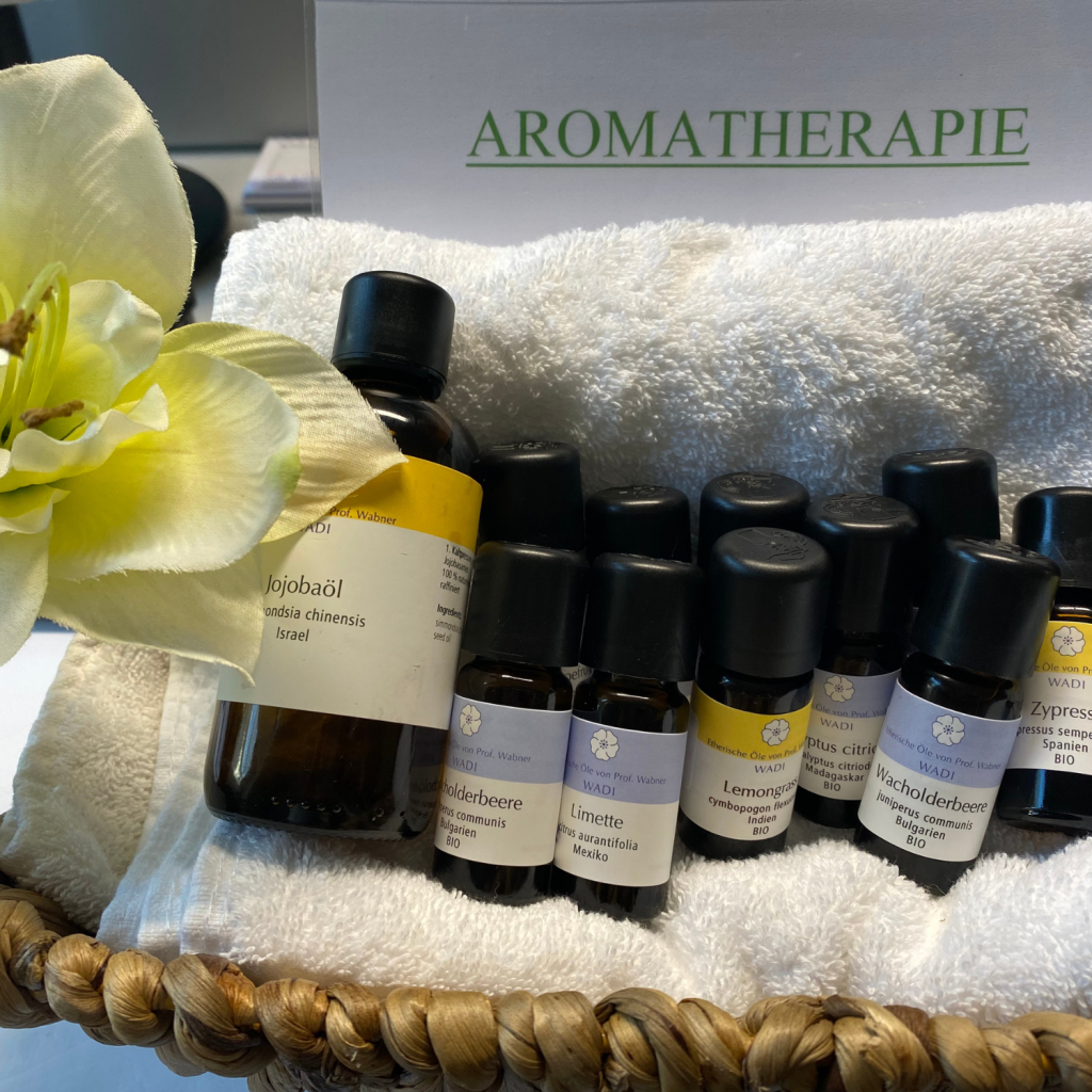 Bild von mehreren Ölen der Aromatherapie, die in einem Korb auf einem Handtuch liegen. Im Hintergrund sieht man ein Schild mit der Aufschrift "Aromatherapie".
