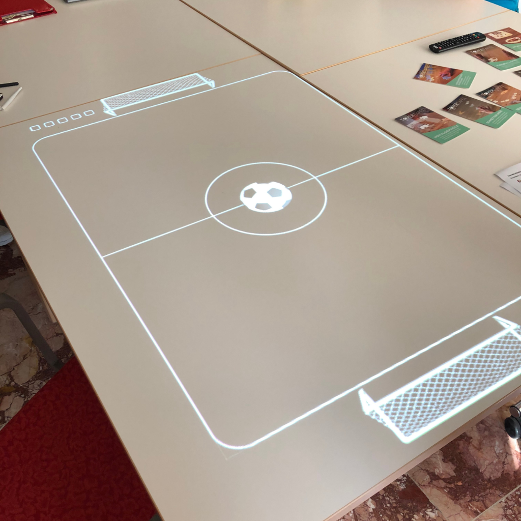 Bild der Tovertafel, die auf einen großen Tisch einer Station ein Fußballspiel abbildet