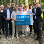 Übergabe der Förderung der Waldtherapie. 55.615€ für das Projekt "Evalution Klinische Waldtherapie bei geriatrischen Patientinnen und Patienten". 2 Personen halten die Förderung in der Hand, dahinter 13 Personen in dem Klinik Wald.